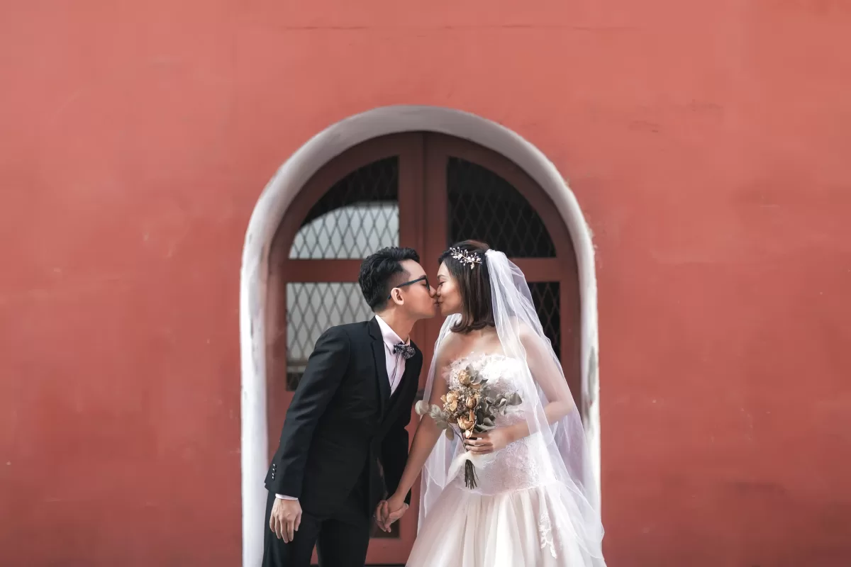 Newlywed couple capturing their love in front of the iconic Melaka Red House. Experience the charm and romance of Melaka as you embark on your journey together. Bridal Melaka - Lees Wedding is here to make your dream wedding a reality with our exquisite gowns and personalized services.